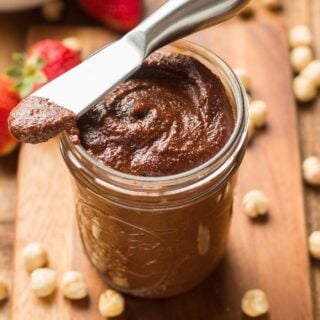 Jar of Vegan Nutella on a Wooden Surface with a Spreader on Top