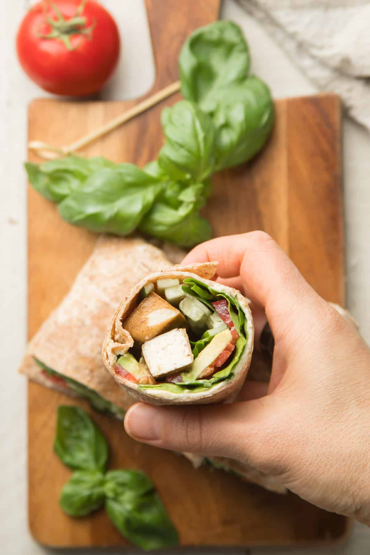 Hand Holding Half of a Vegan Wrap Over a Cutting Board