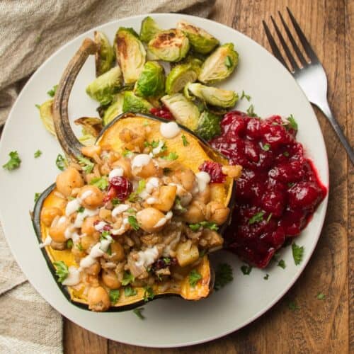 Vegan Stuffed Acorn Squash on a plate with Brussels sprouts and cranberry sauce.