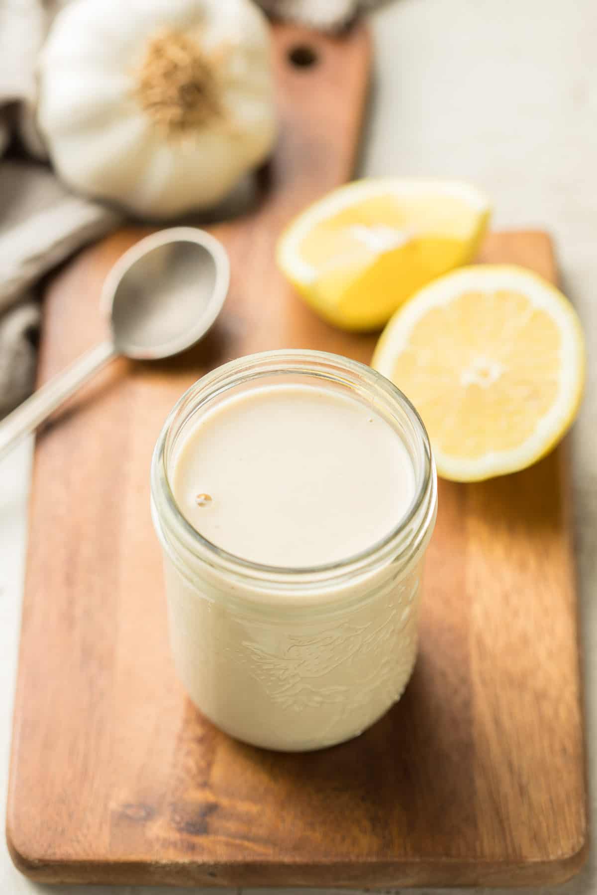 Jar of tahini dressing with lemons and garlic in the background.
