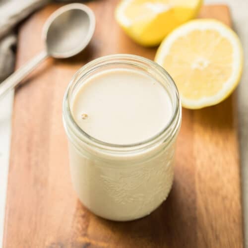 Jar of Tahini Dressing with Lemons and Spoon in the background.