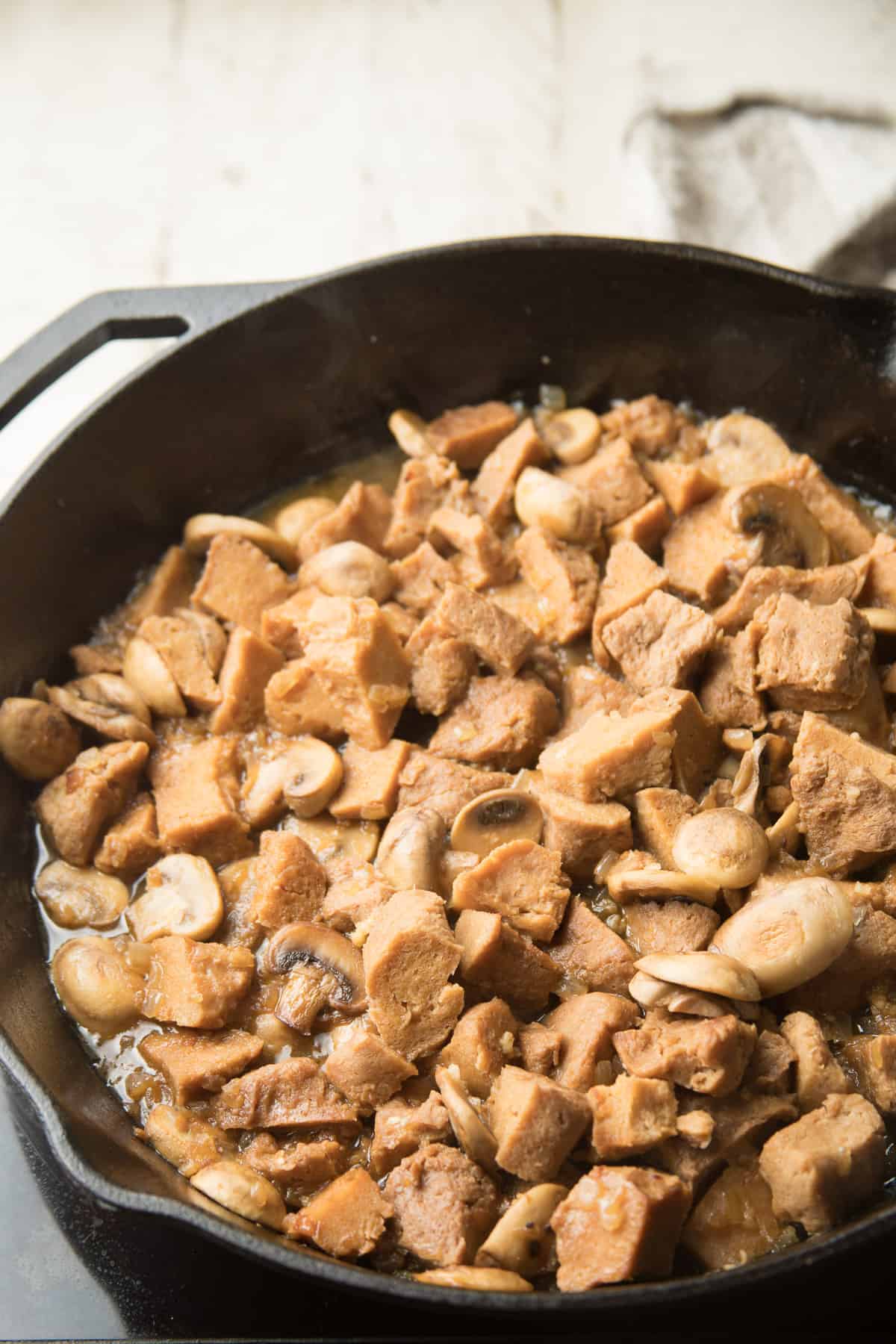 Seitan and mushrooms in a skillet.