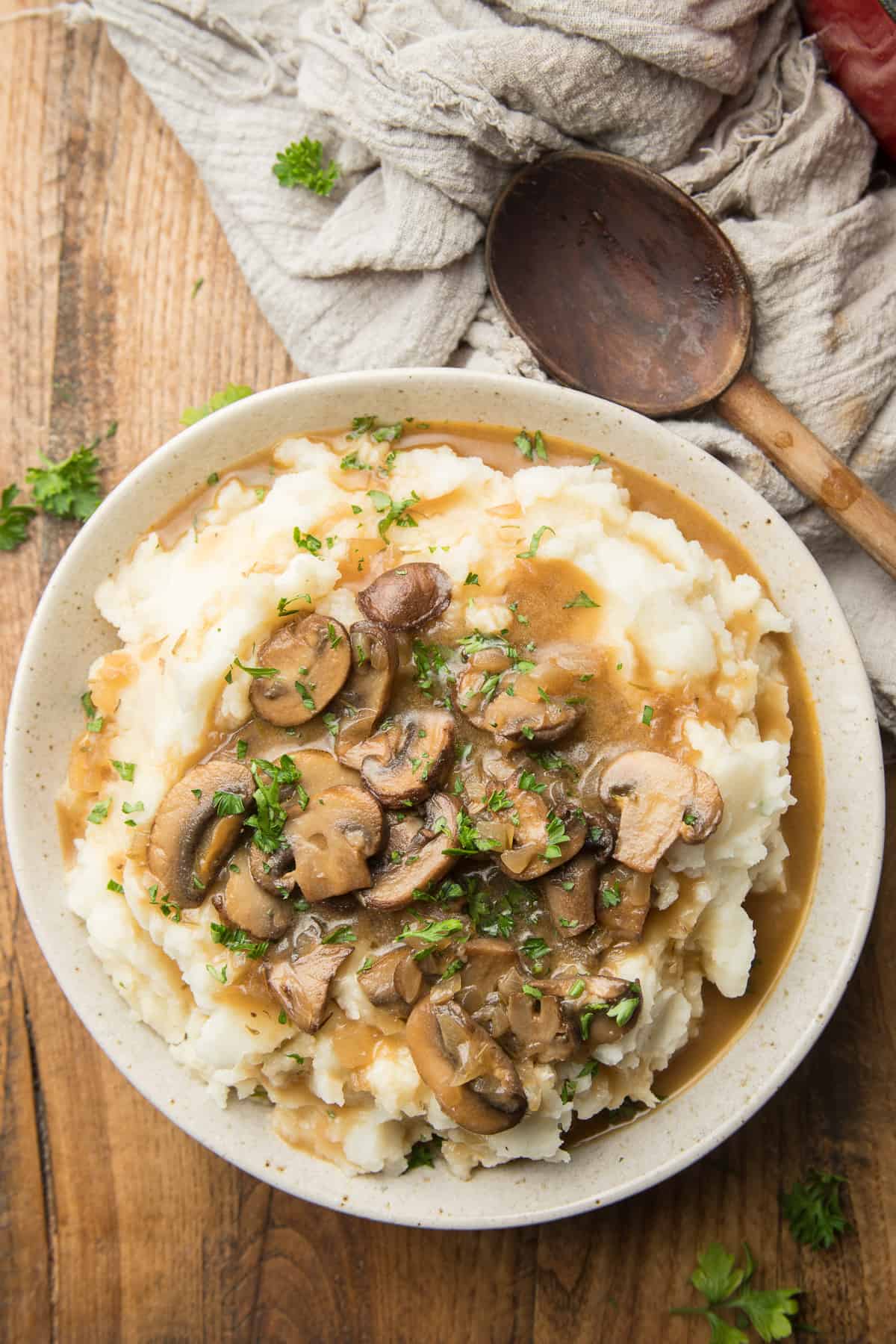 Bowl of Mashed Potaotes and Vegan Mushroom Gravy on a wooden table with wooden spoon on the side.
