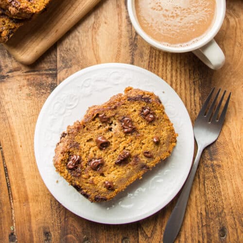 Slice of Vegan Pumpkin Bread on a Plate with Coffee Cup and Fork on the Side.