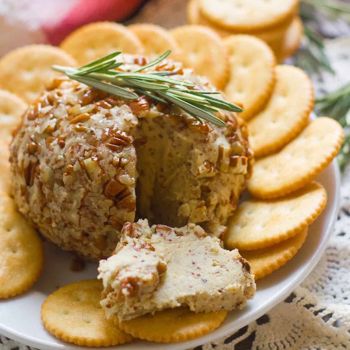 Vegan Cheese Ball with a Slice Cut out and Spread on a Cracker in the Foreground.
