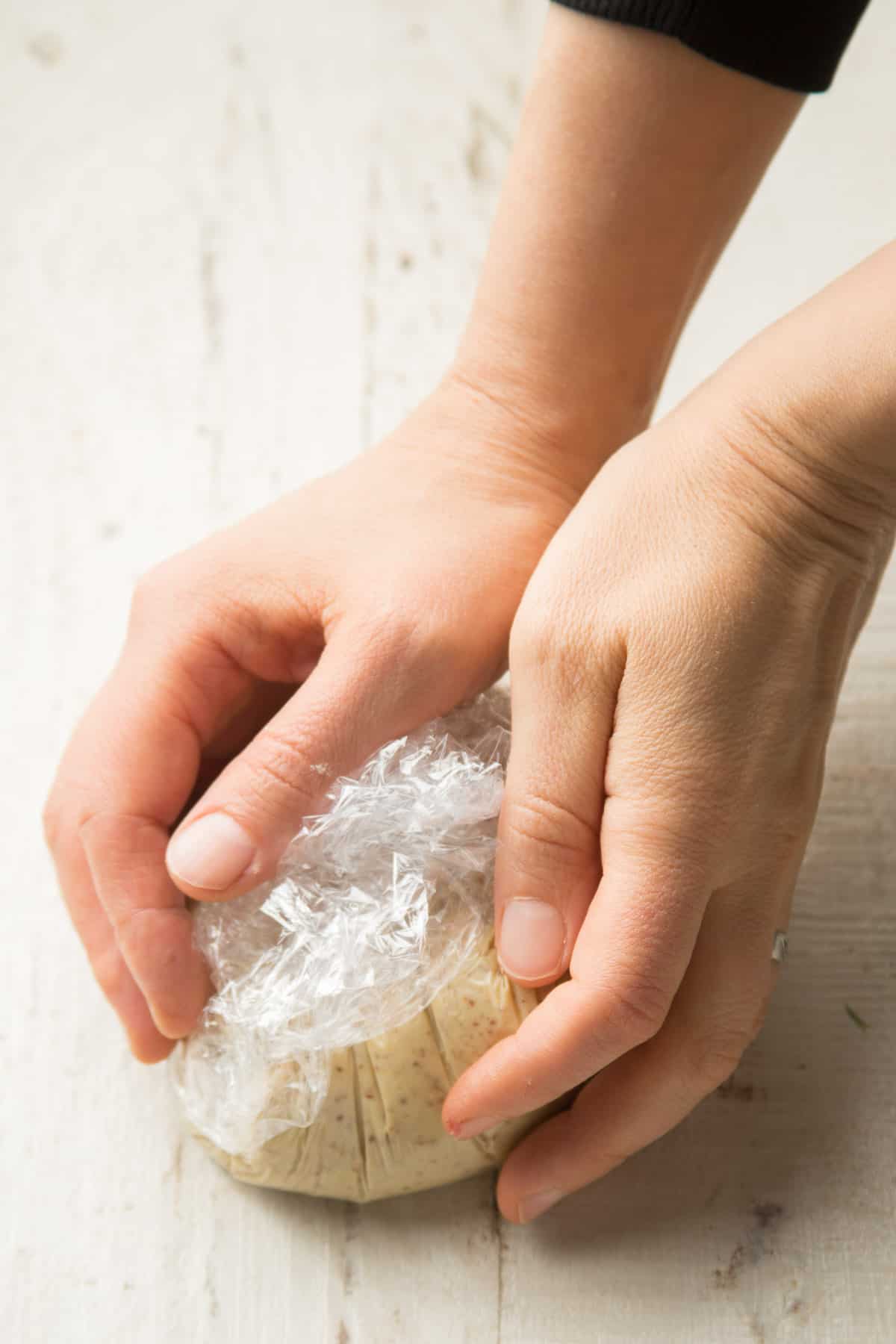 Hands Shaping a Plastic Wrapped Vegan Cheese Ball.