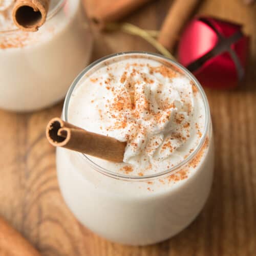 Glass of Vegan Eggnog Garnished with Whipped Cream and a cinnamon stick.
