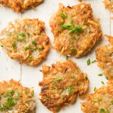 Vegan Potato Latkes Topped with Chives on a White Wooden Surface.