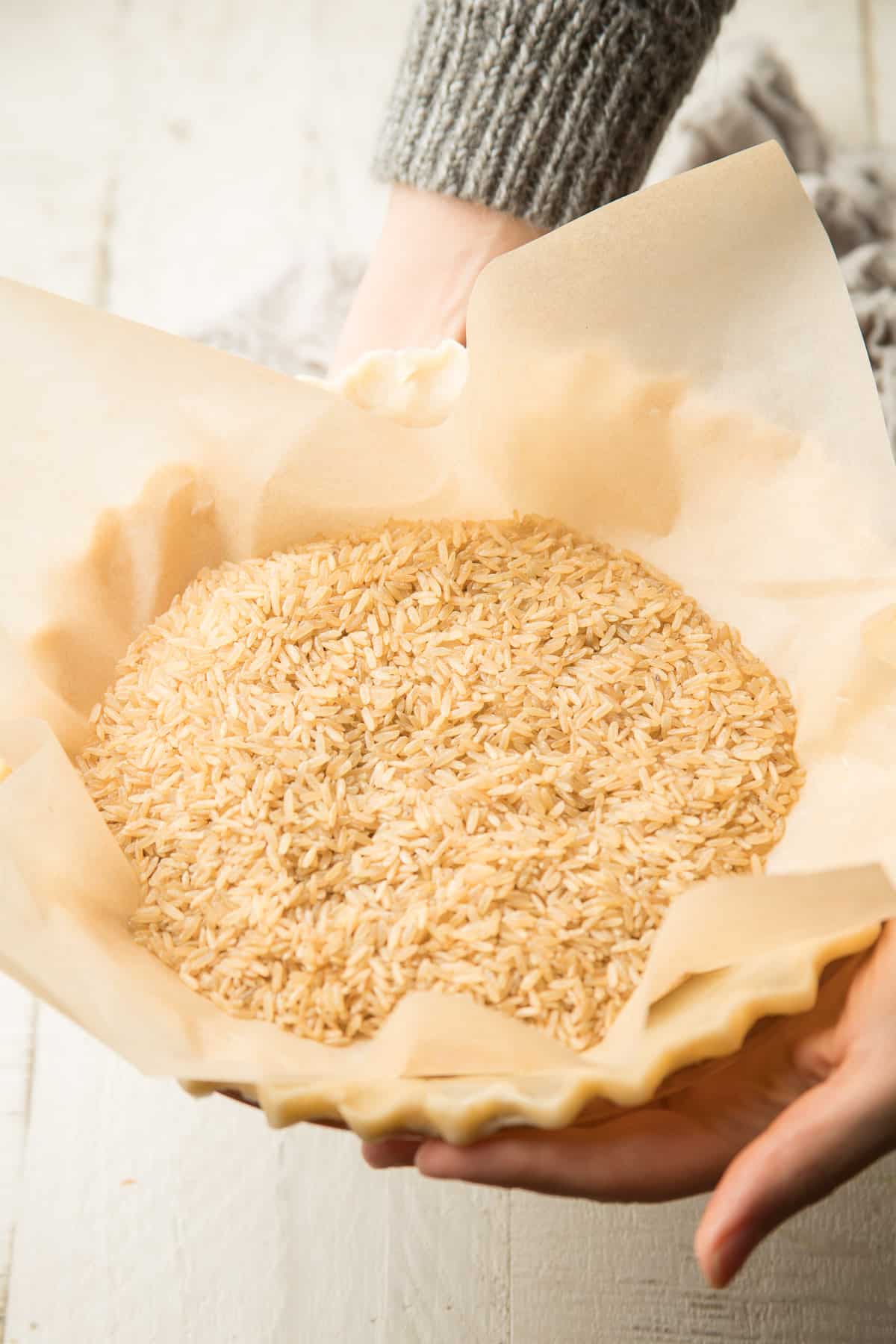 Hands holding a pie crust filled with rice.