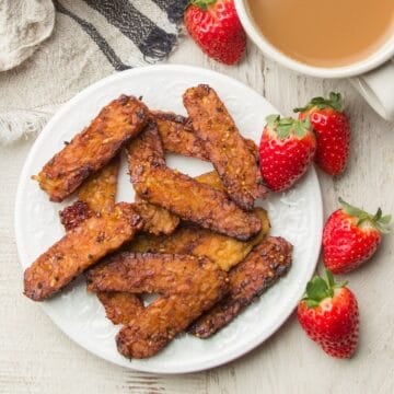 Plate of Tempeh bacon and coffee cup with strawberries on the side.