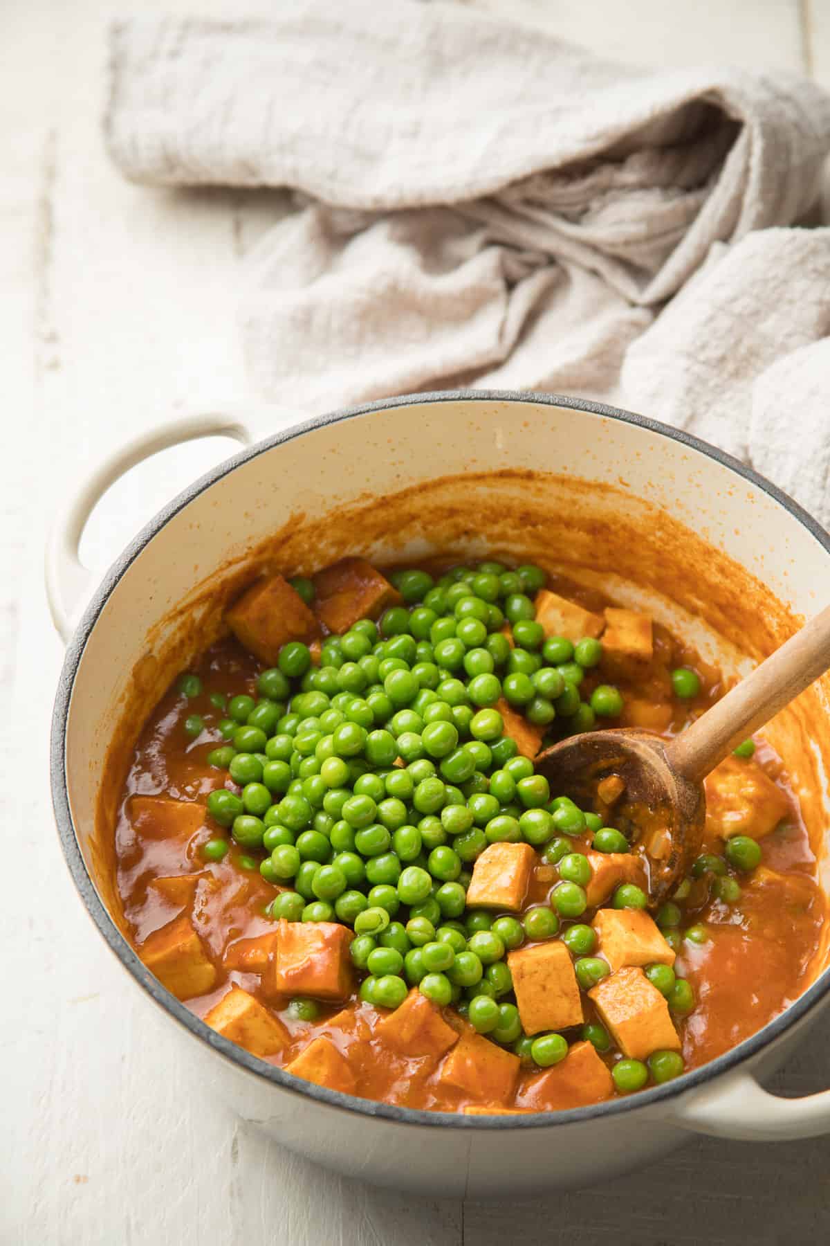 Pot of Tofu curry with a bunch of peas being stirred in.