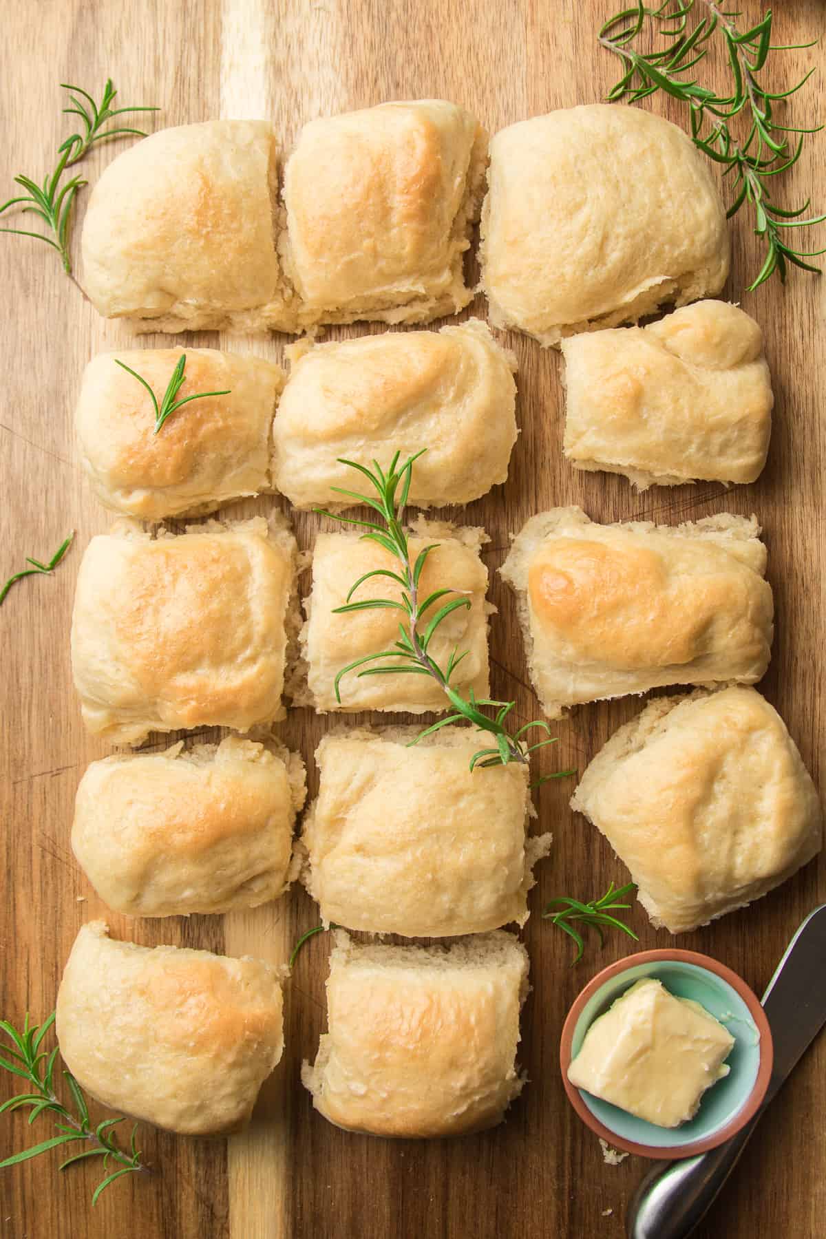 Vegan Dinner Rolls on a cutting board with rosemary and a dish of butter.