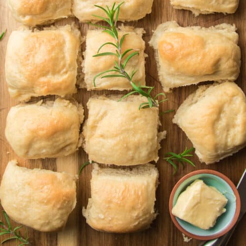 Vegan Dinner Rolls and fresh rosemary arranged on a cutting board with a dish of butter.