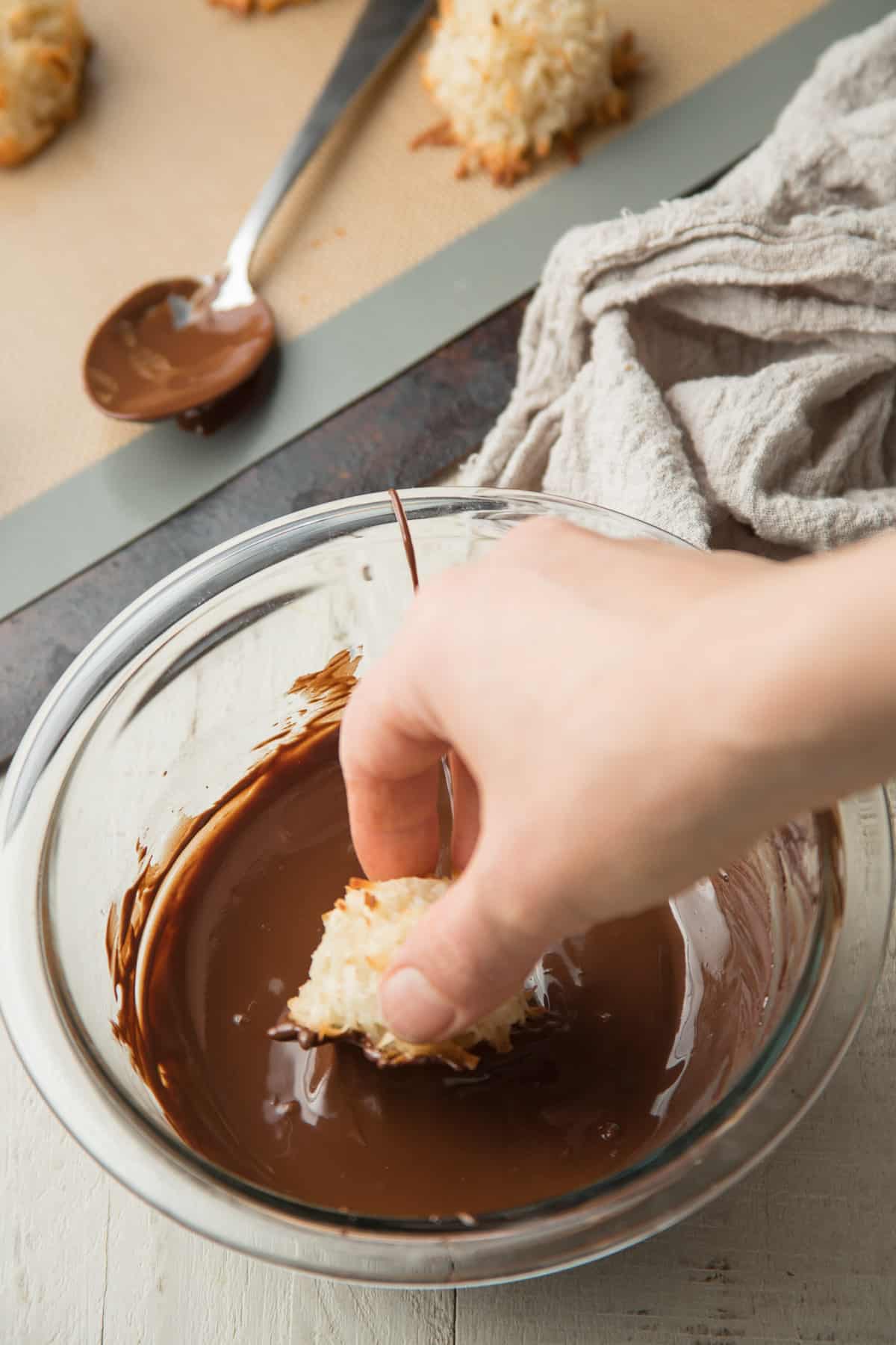 Hand dipping a Vegan Coconut Macaroon in chocolate.