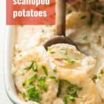Hand scooping Vegan Scalloped Potatoes from a dish with a wooden spoon with text overlay reading "Vegan Scalloped Potatoes".