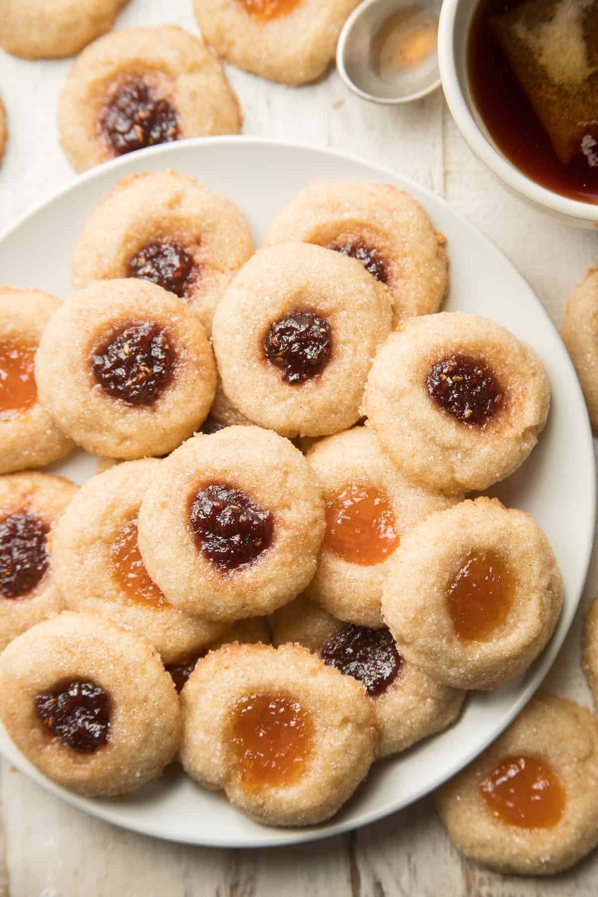 Dish of Vegan Thumbprint Cookies on a white wooden surface with a cup of tea.