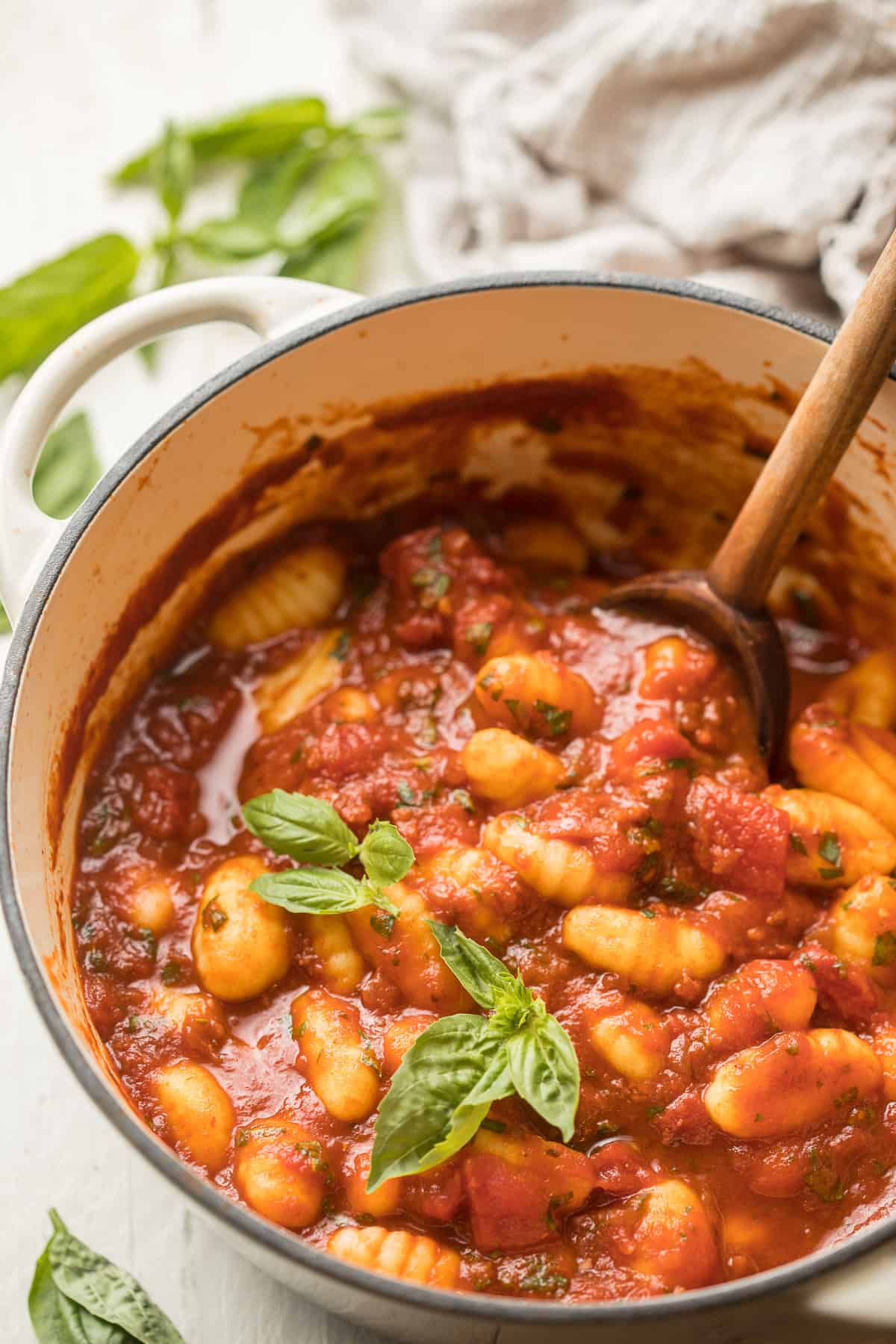 Pot of tomato gnocchi with wooden spoon and fresh basil leaves on top.