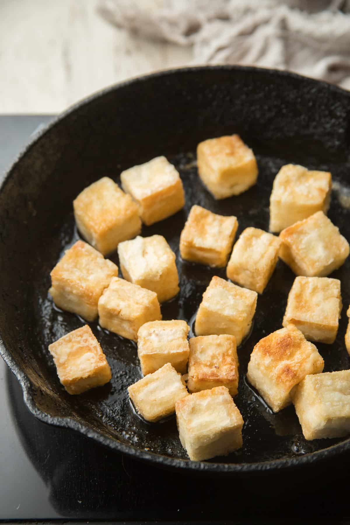 Tofu pieces frying in a skillet.