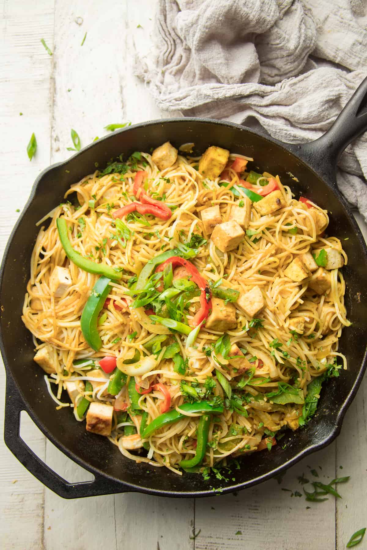 Skillet of Vegan Singapore Noodles on a white wooden surface.