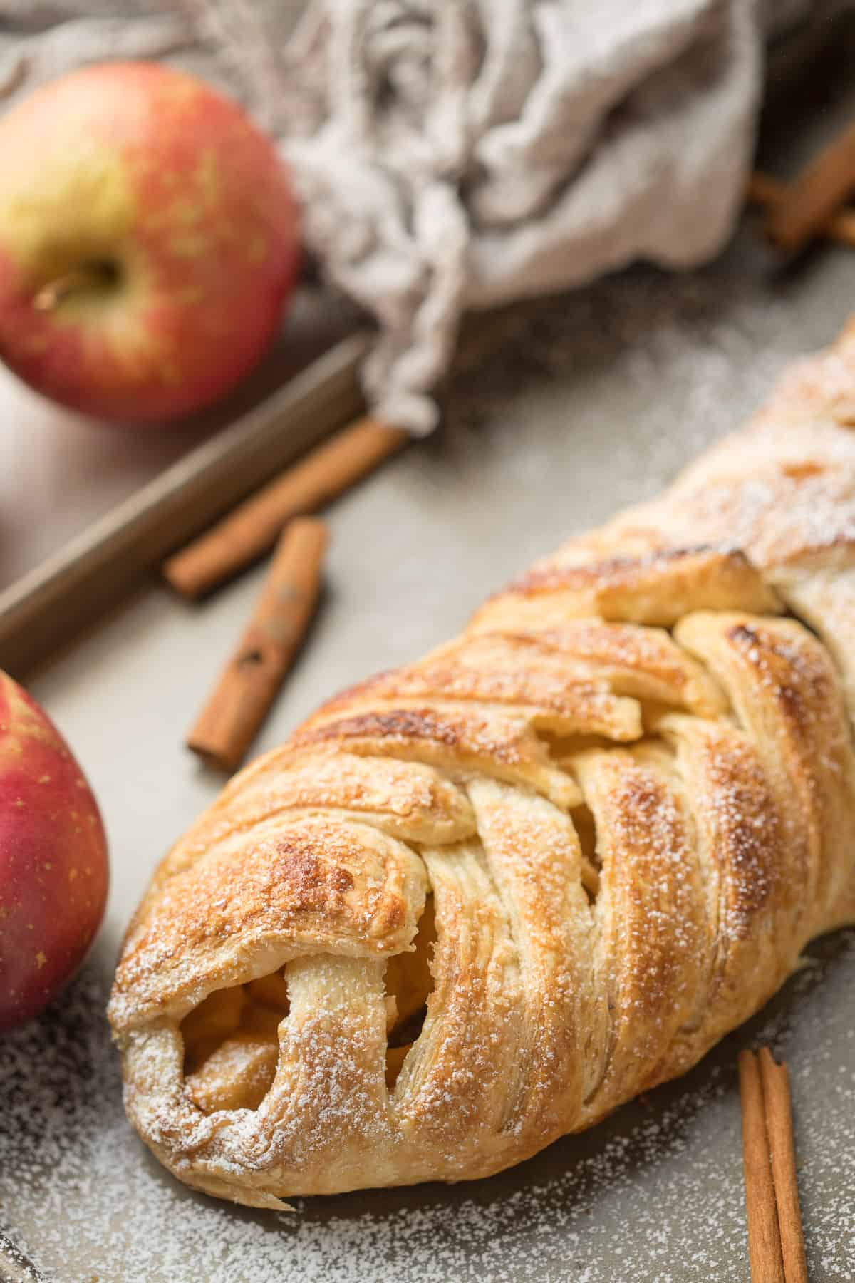 Vegan Apple Strudel on a baking sheet with apples and cinnamon sticks.