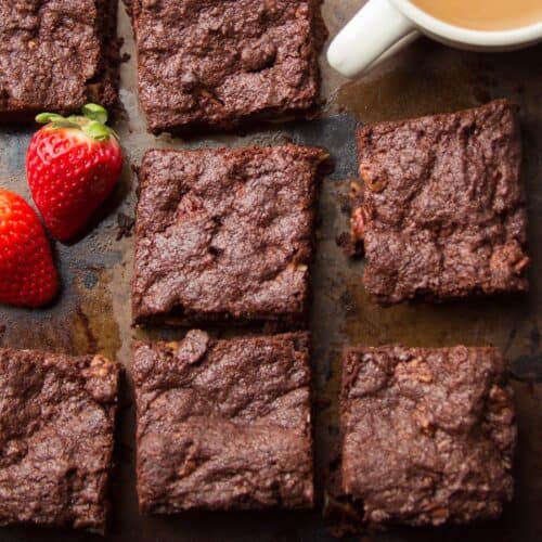 Vegan Brownies on a rustic surface with strawberries and a cup of coffee.