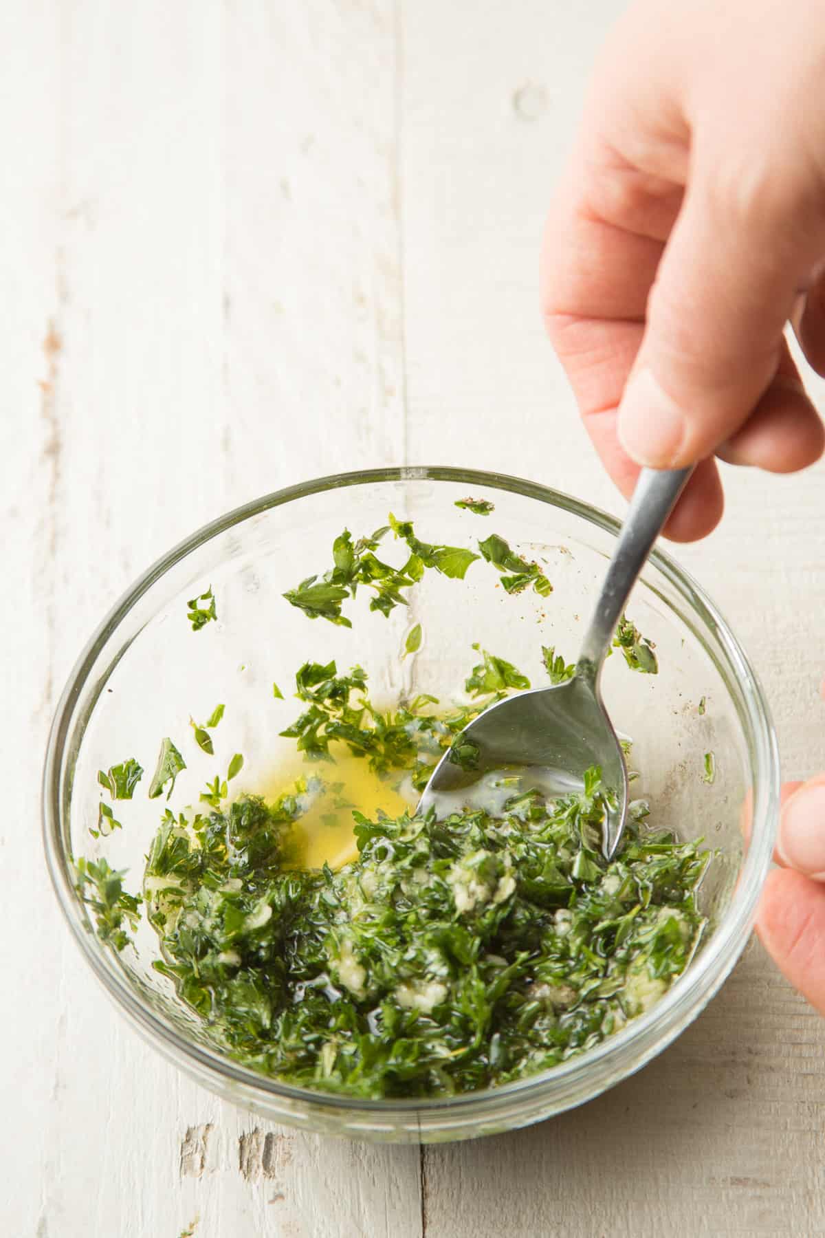 Hand stirring herbs and oil together in a bowl.