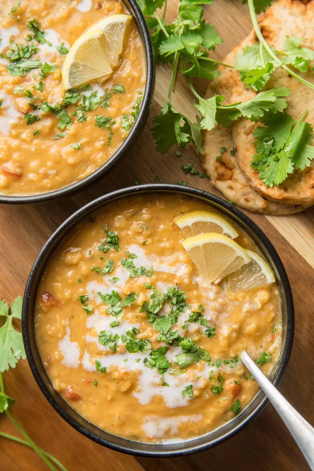 Two bowls of Dal Soup on a wooden surface with fresh cilantro and naan.