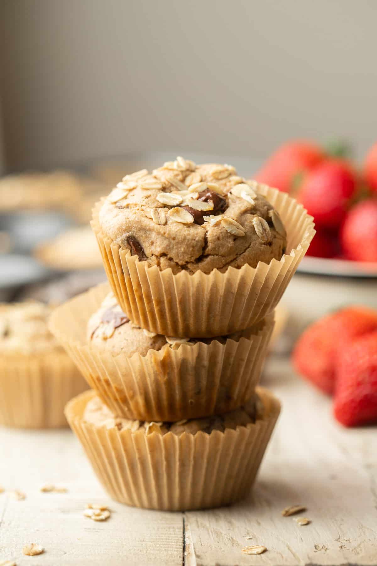Stack of three oat flour muffins with strawberries in the background.
