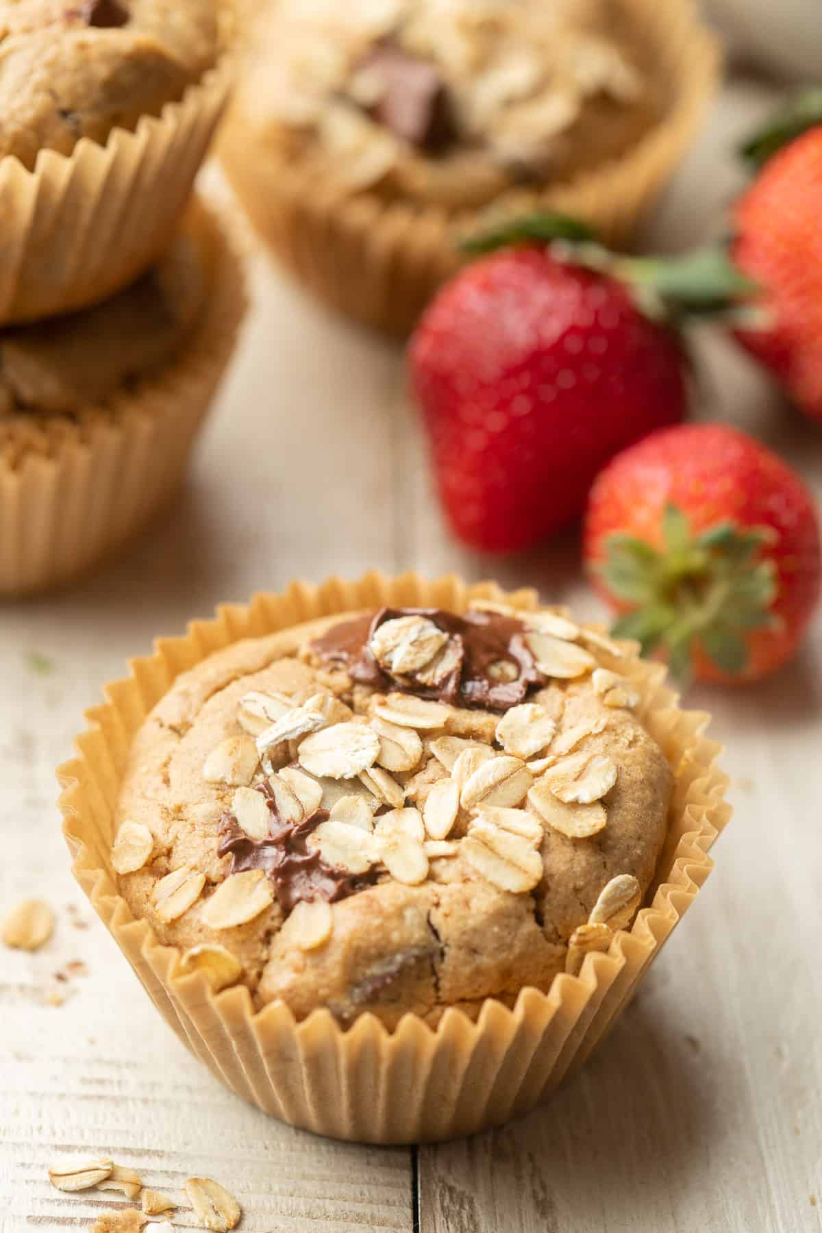 Chocolate Chip Oat Flour Muffins and strawberries on a white wooden surface.