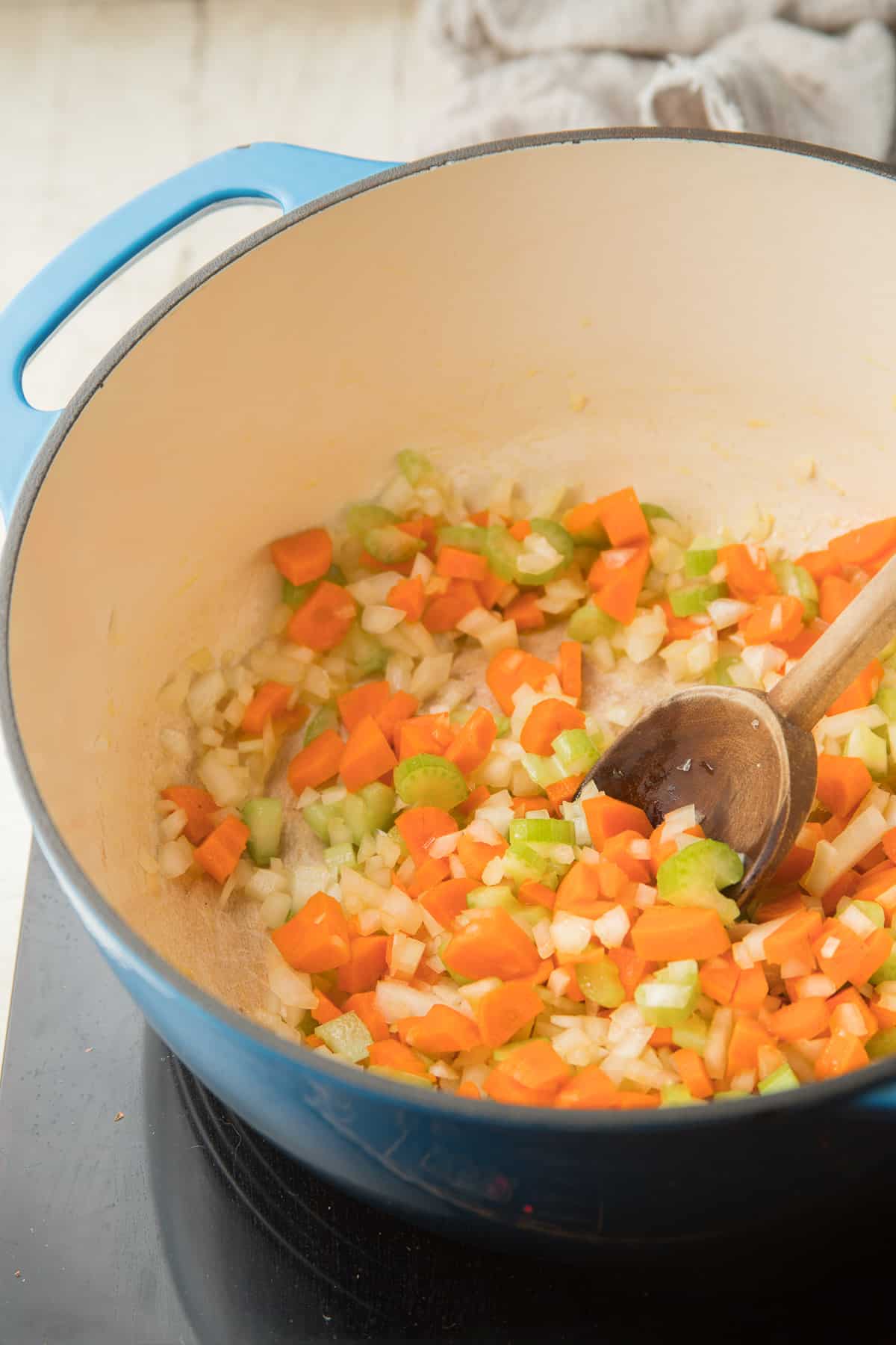 En una cacerola, cocine las cebollas, las zanahorias y el apio con una cuchara de madera.