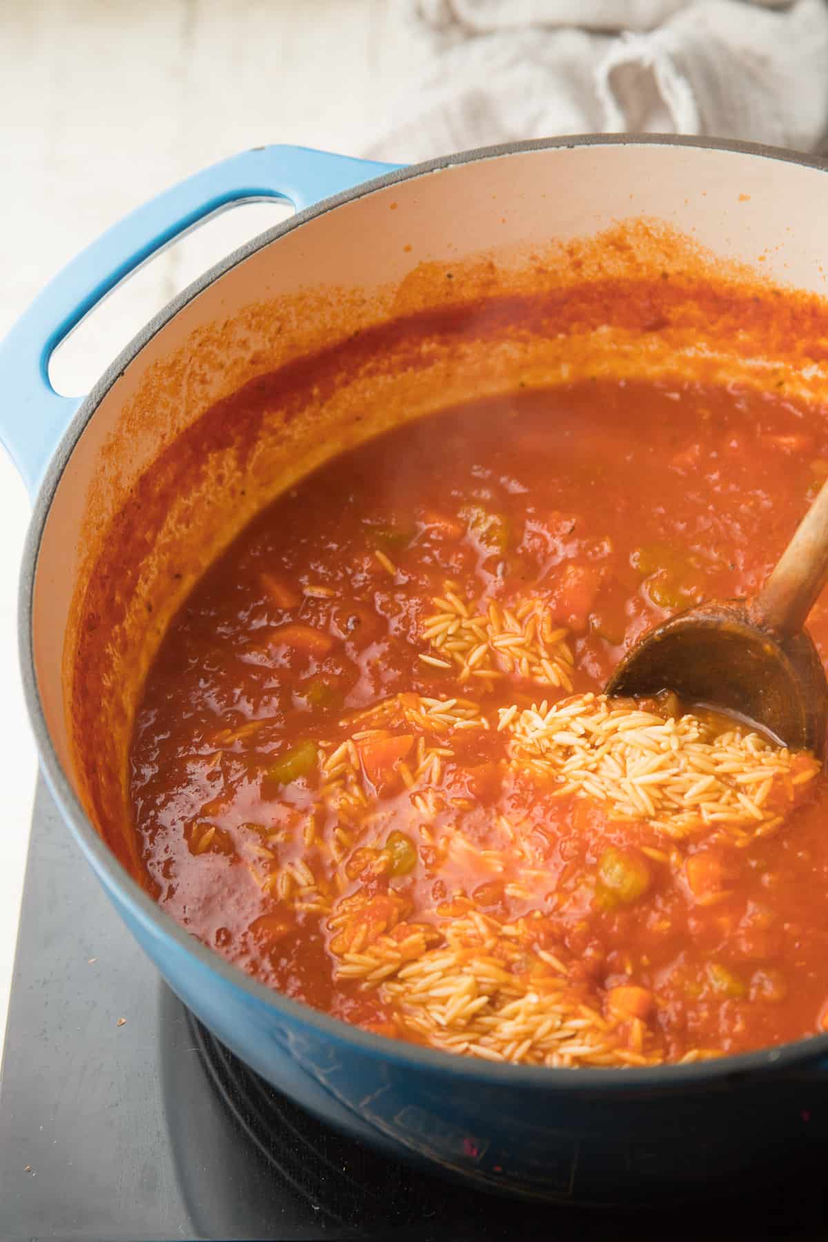 Orzo se revuelve en una olla de sopa de tomate.