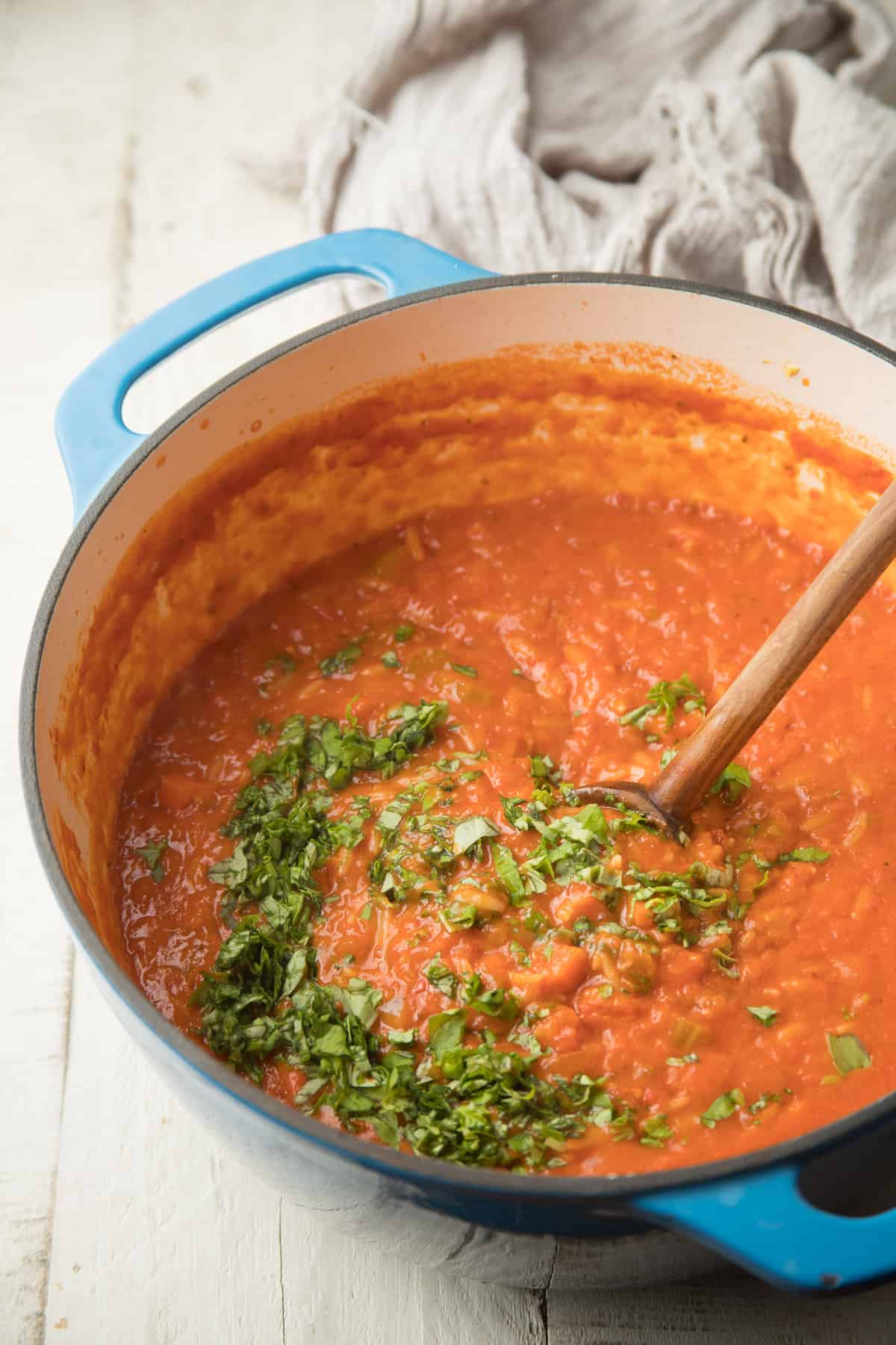 Spoon stirring basil into a pot of Tomato Orzo Soup.