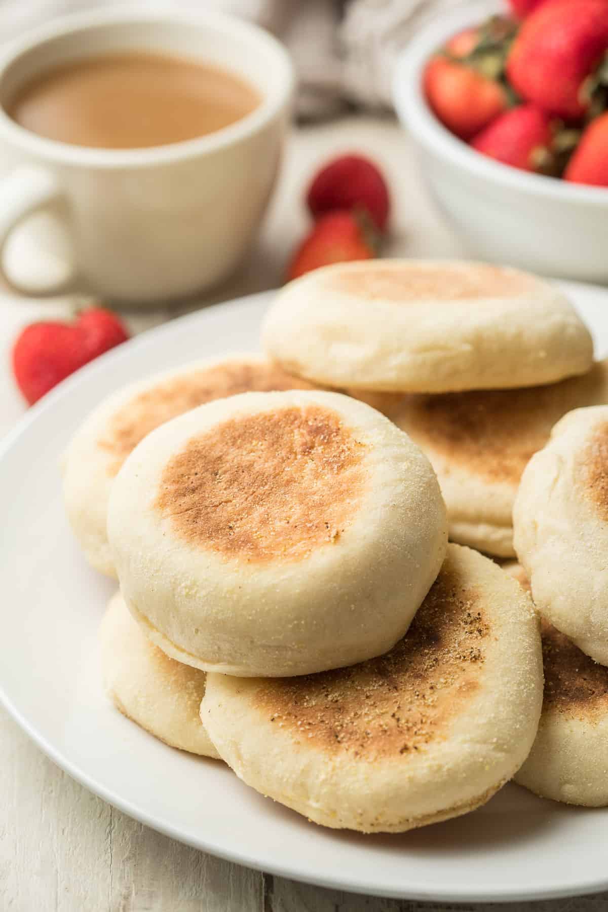 Plate of Vegan English Muffins with coffee cup and strawberries in the background.