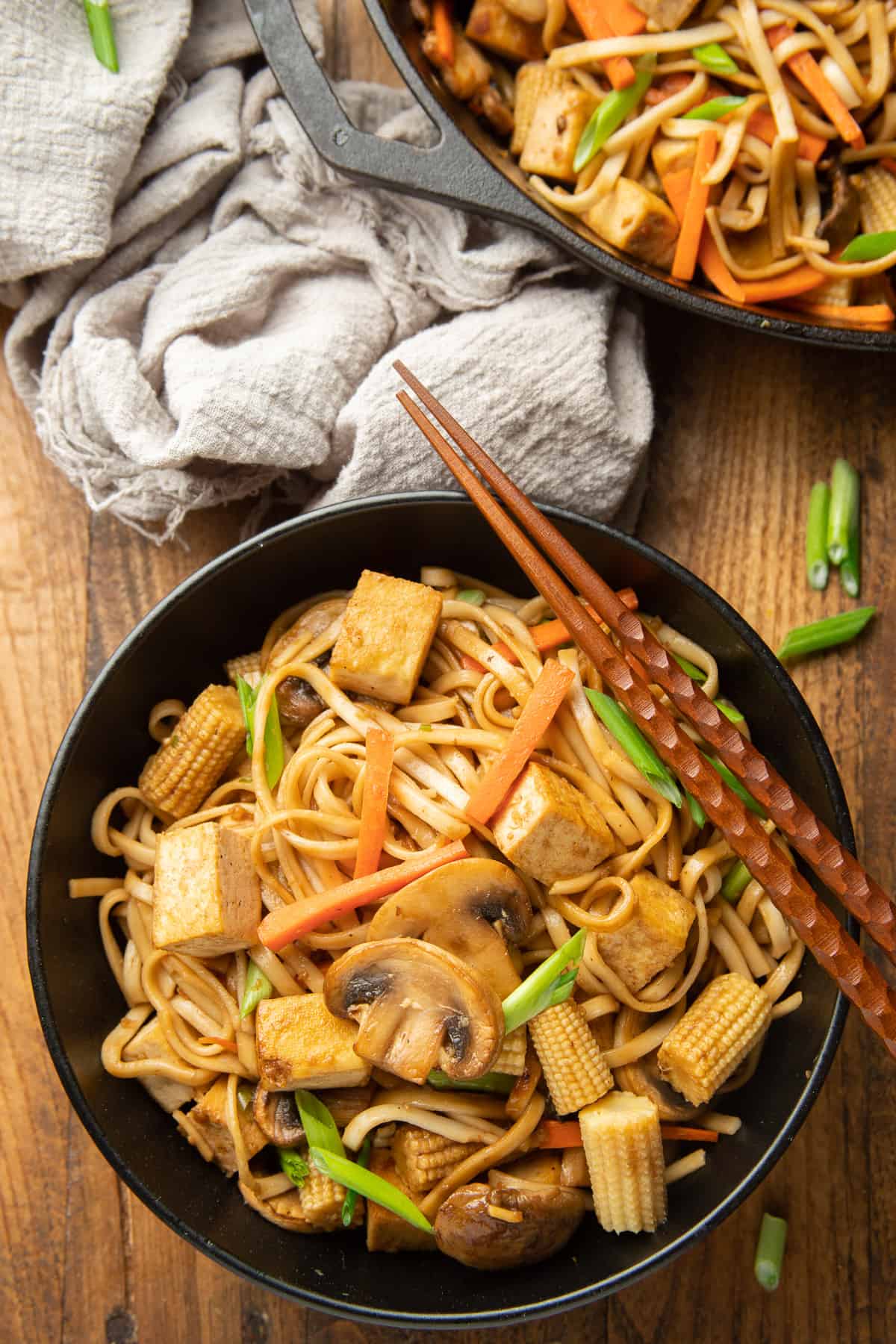 Wooden surface set with skillet, napkin and bowl of Vegan Lo Mein.
