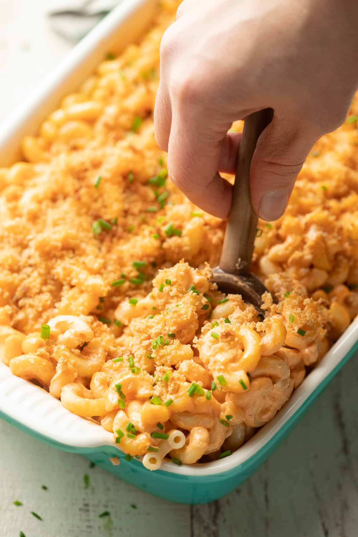 Hand using a spoon to scoop baked Vegan Mac & Cheese from a dish.