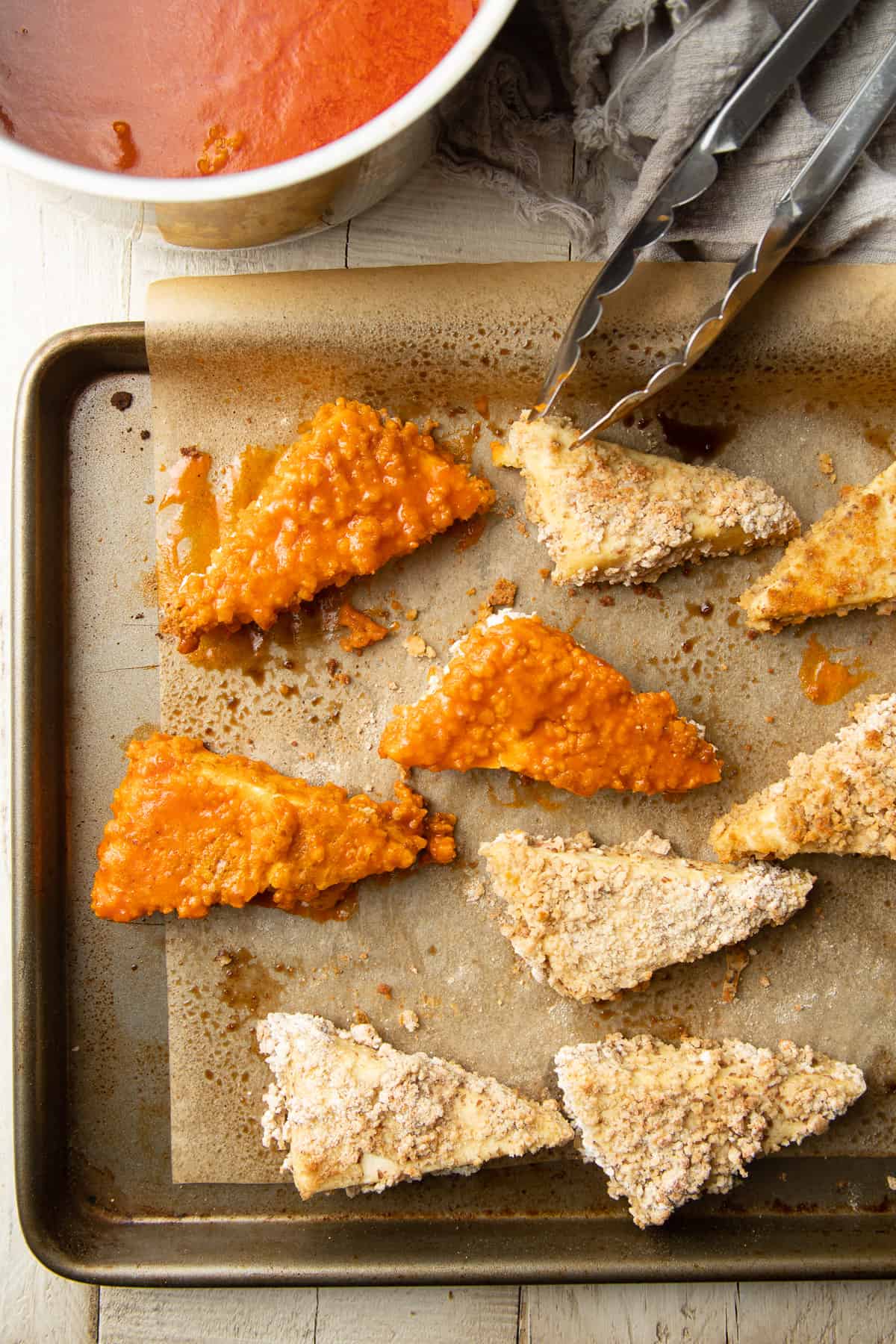 Baked tofu pieces partially dipped in Buffalo sauce and arranged on a baking sheet.