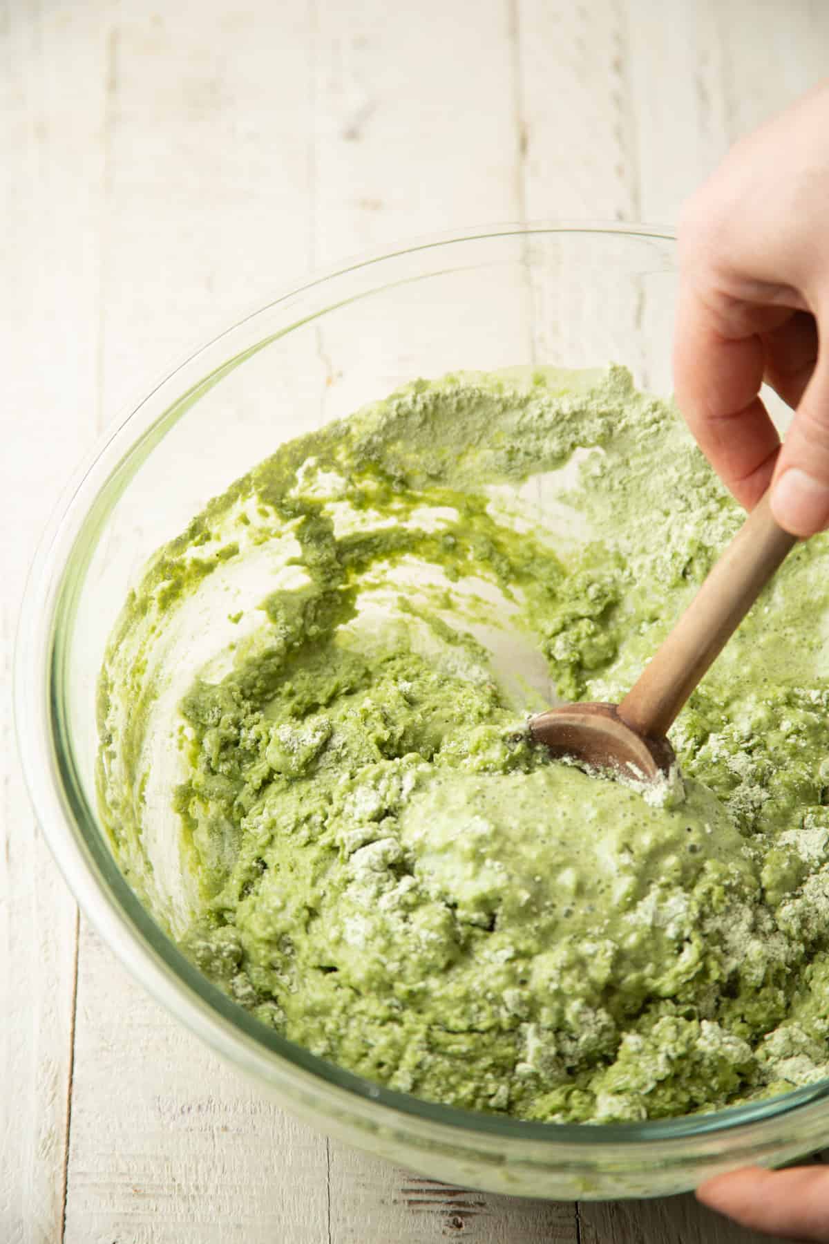 Hand stirring matcha muffin batter in a bowl.