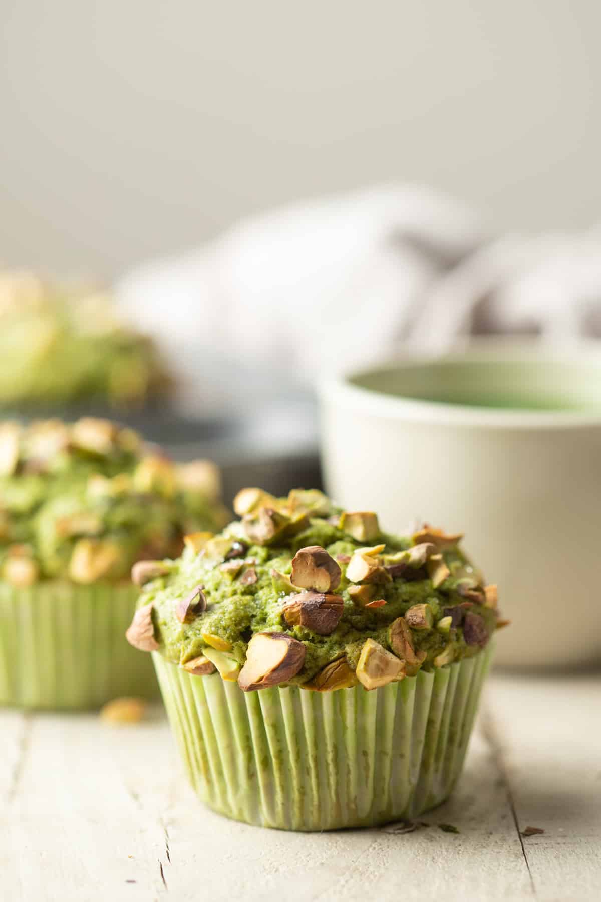 Matcha Pistachio Muffins and tea cup on a white wooden surface.