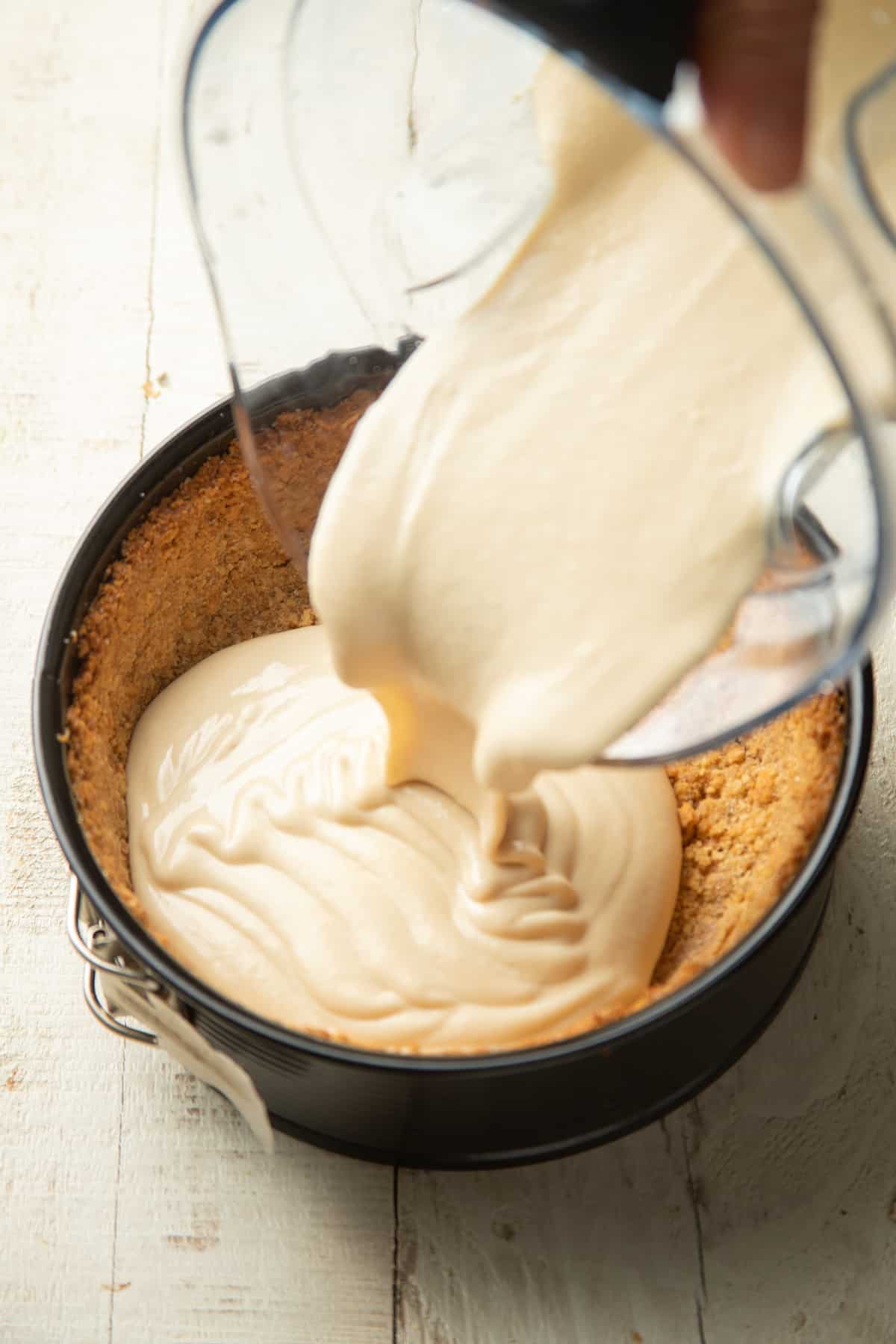Vegan Cheesecake batter being poured from a blender into a crust.