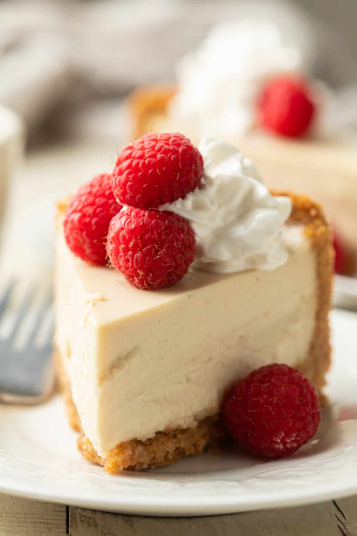 Vegan Cheesecake slice on a plate with raspberries and fork.