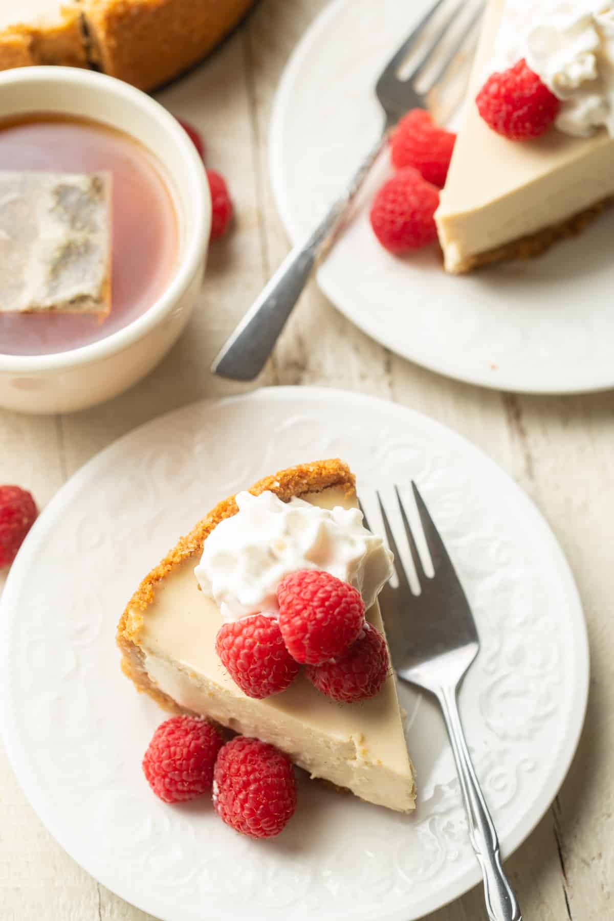 White wooden surface set with tea cup and two slices of Vegan Cheesecake on plates.