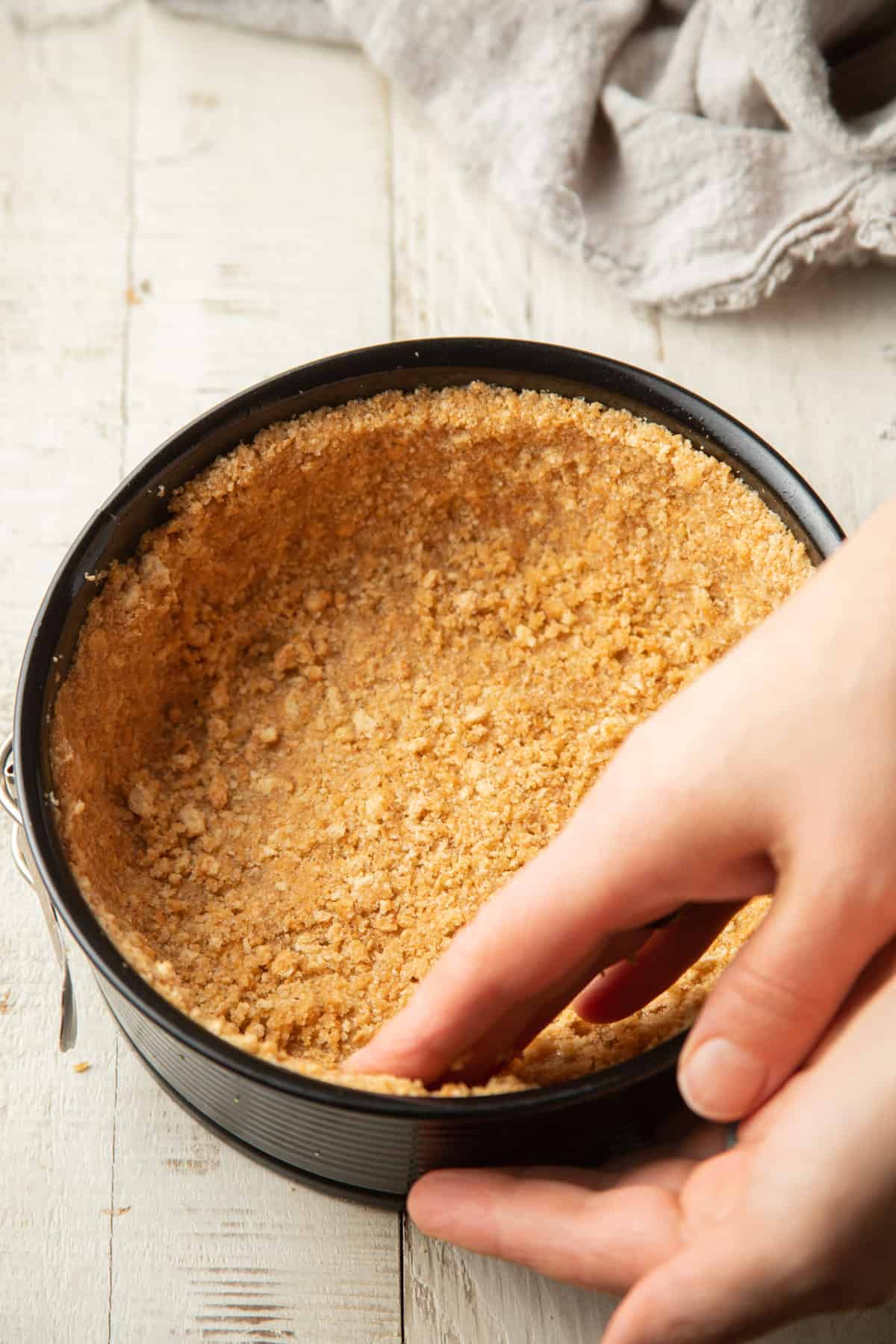 Hand pressing graham cracker crumb mixture into a springform pan.