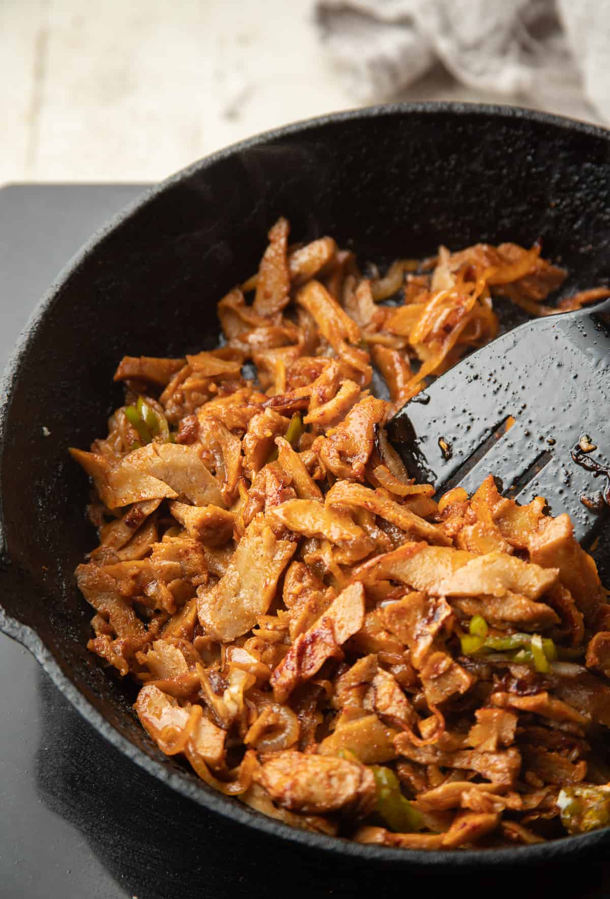 Seitan, onions and peppers sizzling in a skillet.