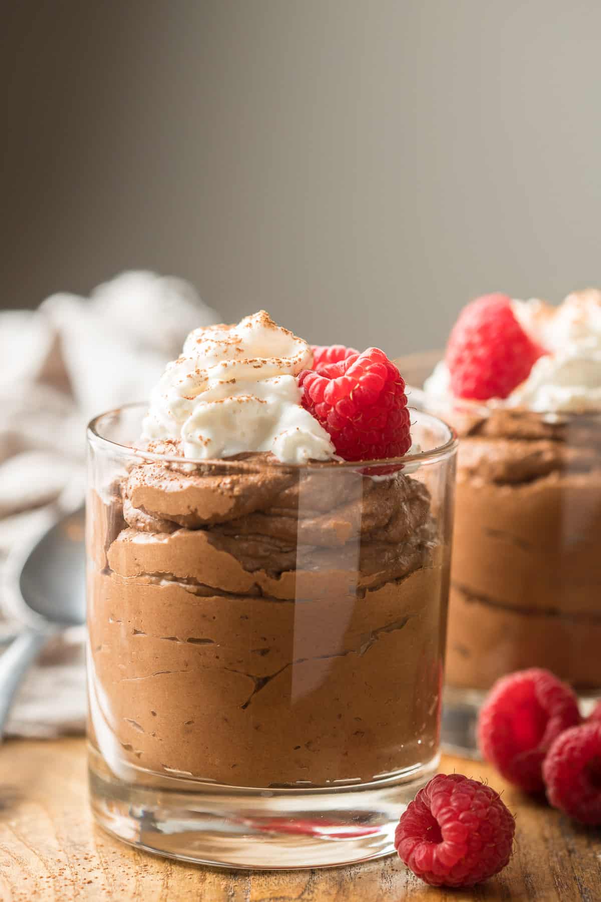 Two glasses of Vegan Chocolate Mousse with raspberries and whipped cream on top.