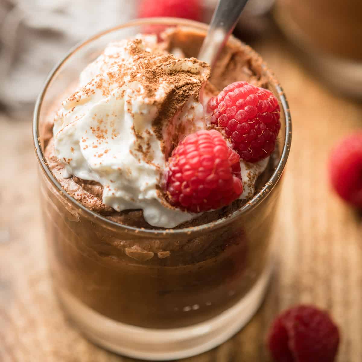 Cup of Vegan Chocolate Mousse with raspberries, whipped cream and cocoa powder on top.