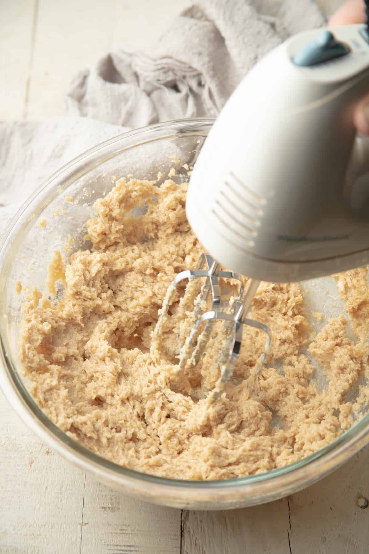 Electric mixer beating butter and sugars in a mixing bowl.