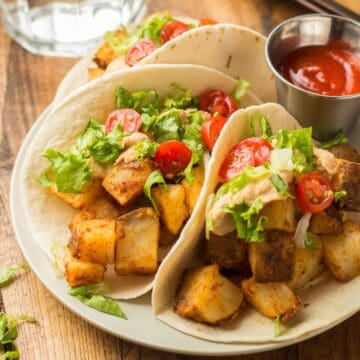 Three potato tacos on a plate with a dish of hot sauce.