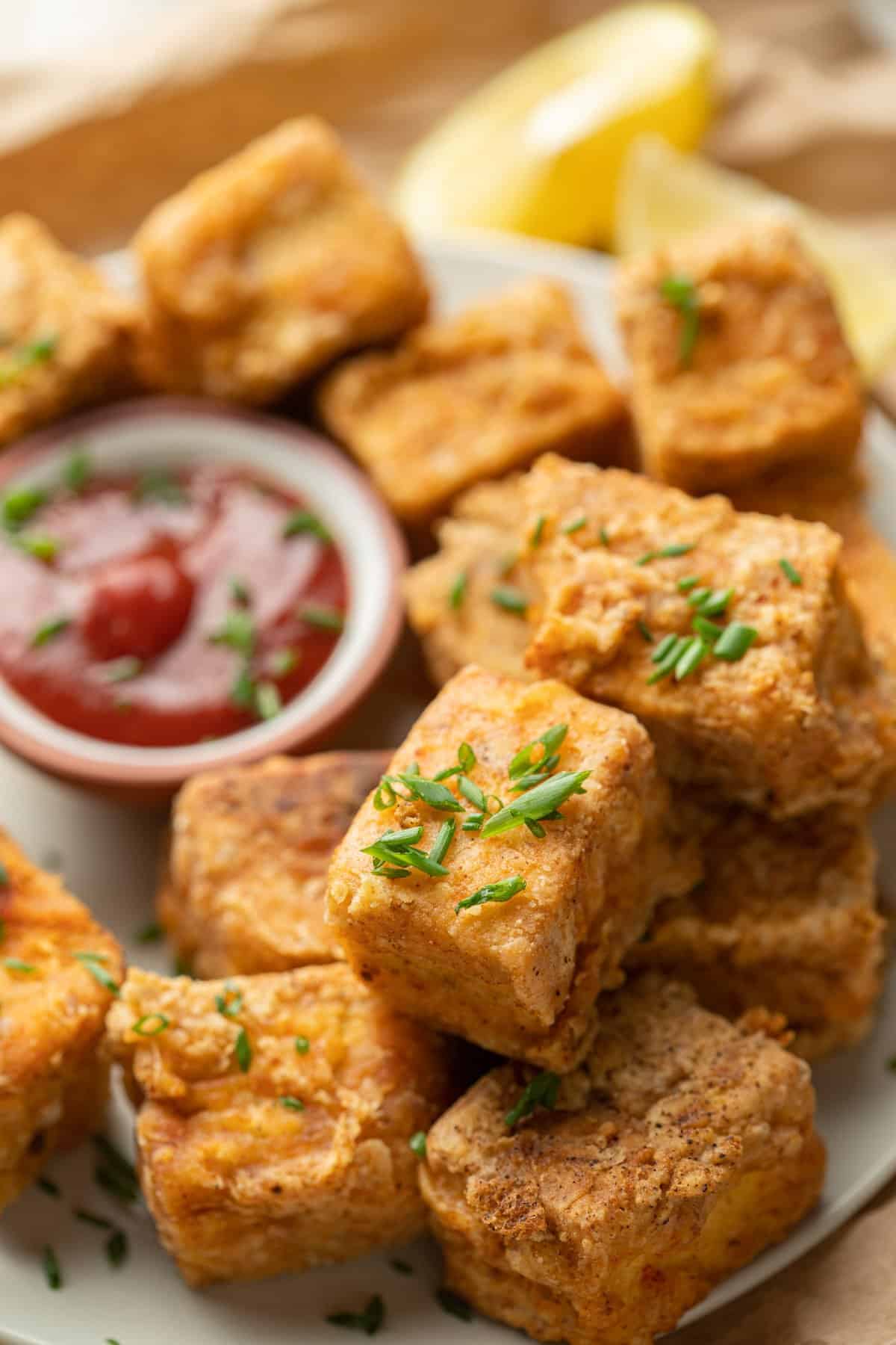 Tofu Chicken Nuggets on a plate with barbecue sauce and lemon slices in the background.