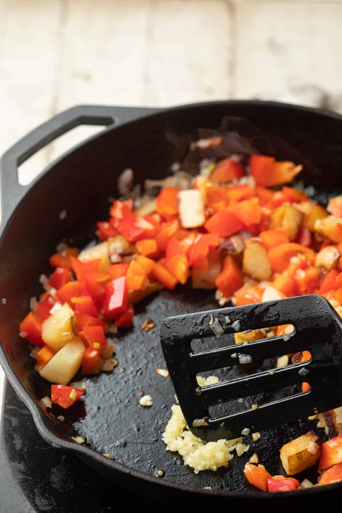 Garlic cooking in a skillet with peppers, potatoes and onions.