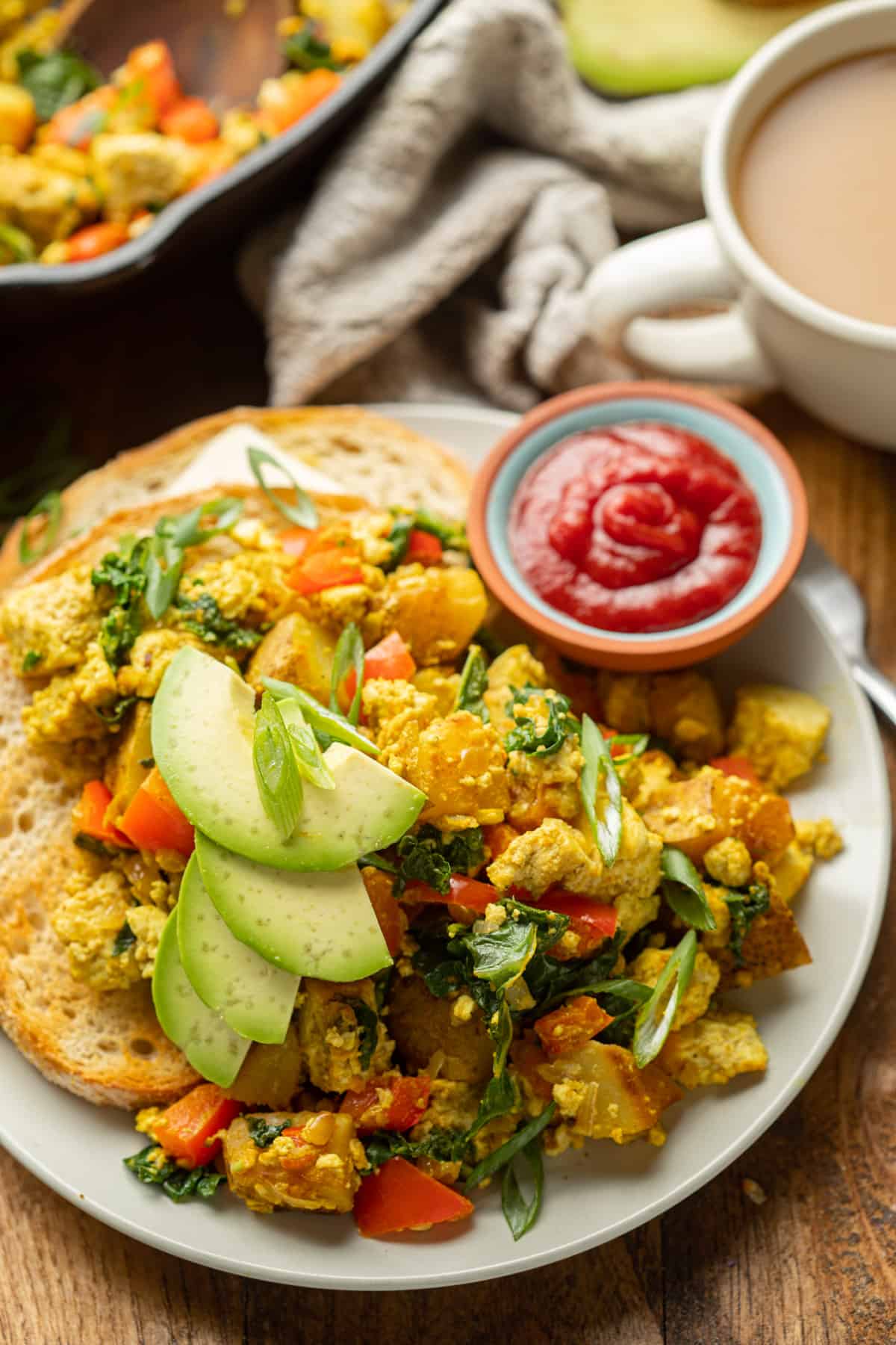 Plate of Tofu Scramble with skillet and coffee cup in the background.